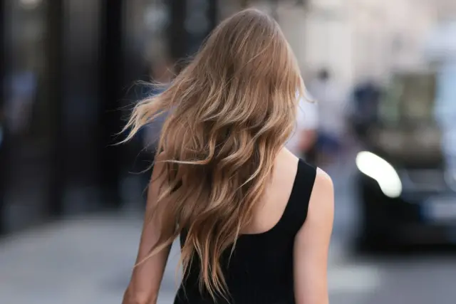 Kobieta z falującymi, blond włosami po perfekcyjnym blowout, idzie ulicą.