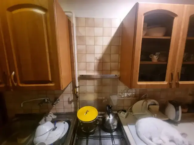 Zabudowa rury gazowej w kuchni, obok szafek i zlewu. Biały kot odpoczywa na blacie.