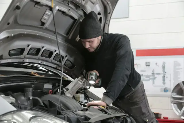 Mechanik z latarką bada silnik Renault, szukając przyczyny błędu DTC P0300.