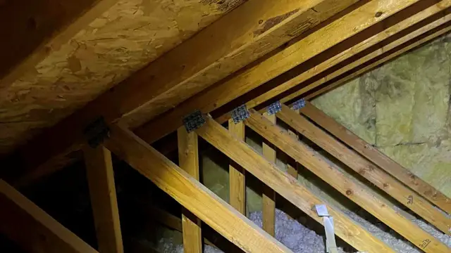 Drewniana konstrukcja dachu z widoczną izolacją. Widać krokwie i przestrzeń między murłatą a dachem, gdzie znajduje się wełna mineralna.