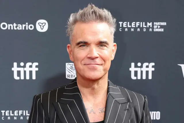 Robbie Williams, znany również jako aktor, w stylowej marynarce w paski na tle logo TIFF.