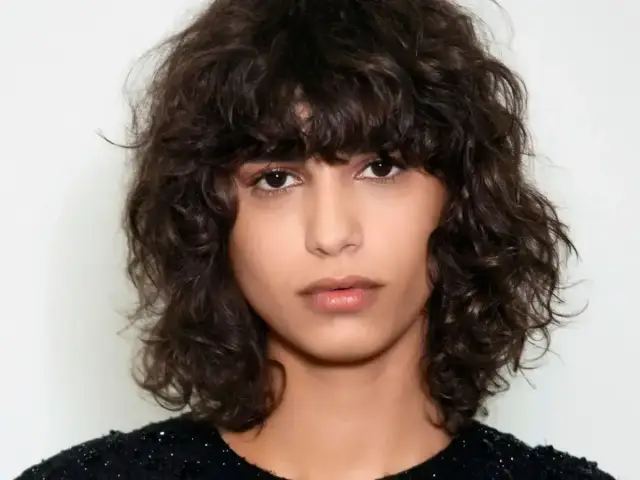 Kobieta z burzą ciemnych, kręconych włosów w stylu bob. Jej loki tworzą naturalną, swobodną fryzurę.