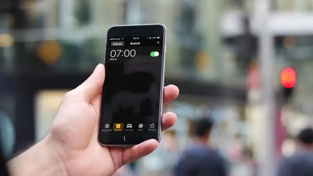 Dłoń trzyma iPhone'a z włączonym budzikiem na godzinę 07:00.