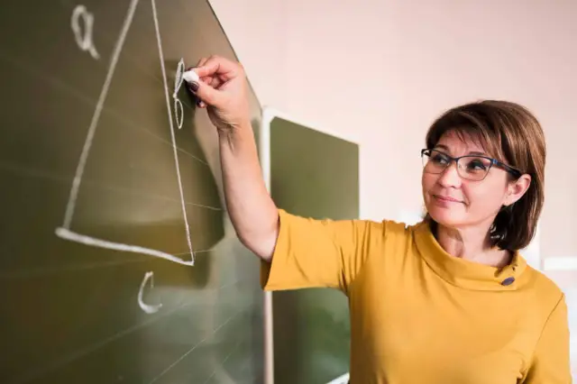 Nauczycielka pisze kredą na tablicy. Taka osoba, jak ona, może pracować w świetlicy szkolnej, pomagając dzieciom w nauce.