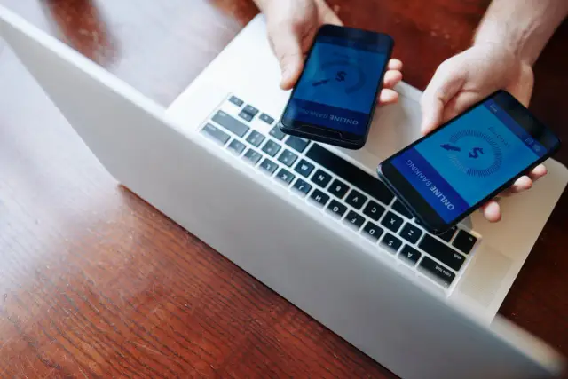 Dwie dłonie trzymają telefony z aplikacją bankową, gotowe do płatności. Szybkie przelewy jak paypal blik.