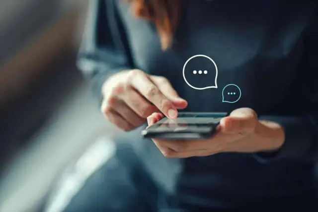 Dłonie trzymające smartfon, na ekranie widoczne ikony czatu. Zastanawiasz się, jak wysłać anonimowy SMS?