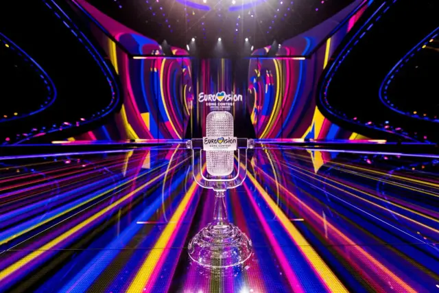 Kryształowy mikrofon na scenie Eurowizji, gotowy na występy Wielkiej Piątki. Kolorowe światła tworzą magiczną atmosferę.