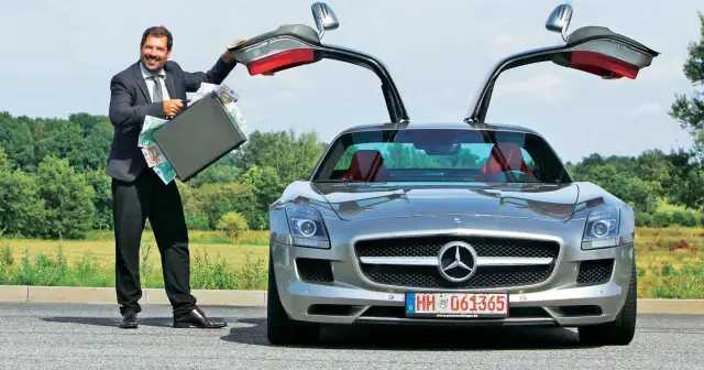 Szczęśliwy mężczyzna w garniturze otwiera drzwi swojego SLS AMG, prezentując walizkę pełną pieniędzy.
