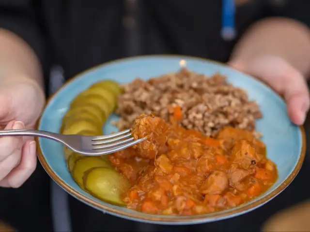 Gulasz z kaszą gryczaną, ogórki kiszone i widelec nabierający kawałek mięsa. Pyszny, sycący obiad.