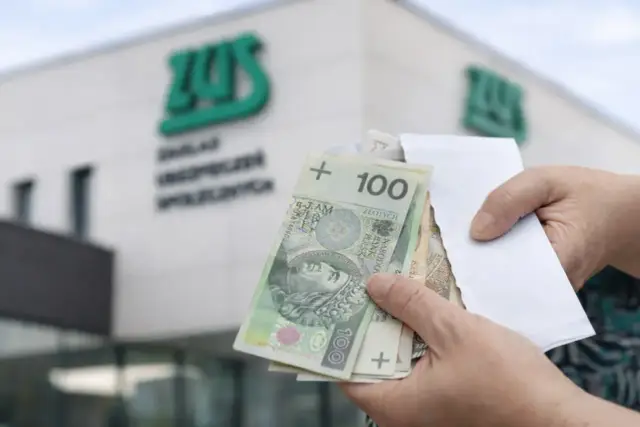 Ręce trzymają polskie banknoty przed budynkiem ZUS. Kiedy najlepiej przejść na emeryturę w 2026 roku?