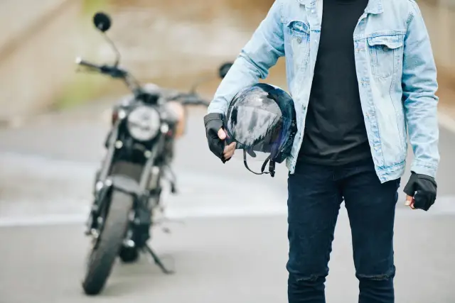 Gotowy na jazdę nowym motocyklem. W ręku trzyma kask, ubrany w jeansową kurtkę i rękawiczki.