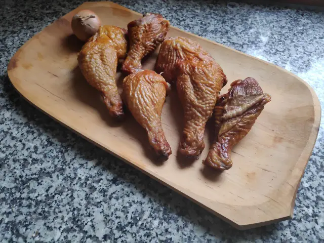 Na drewnianej desce leżą apetyczne, wędzone udka z kurczaka bez parzenia. Obok leży cebula.