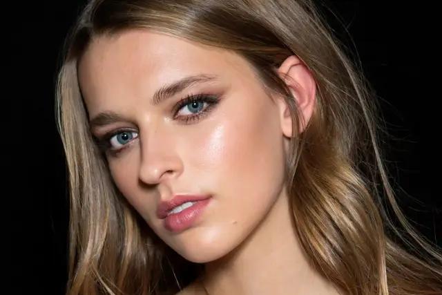 Modelka z błękitnymi oczami i subtelnym makijażem, jej włosy w odcieniu flamboyage mienią się w świetle.