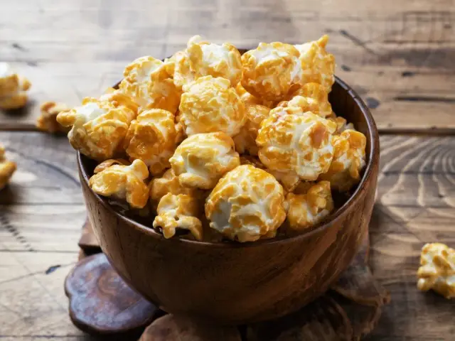 Drewniana miska pełna karmelowego popcornu na drewnianym tle.