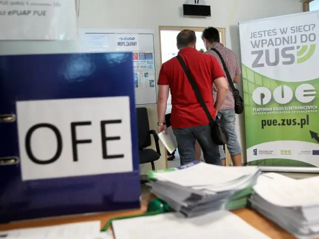 Niebieska teczka z napisem OFE stoi na biurku obok stosów dokumentów. W tle mężczyźni wchodzą do urzędu ZUS, gdzie wisi baner zachęcający do korzystania z platformy PUE.