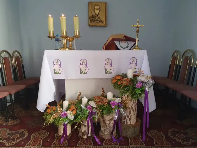 Ołtarz kościelny ozdobiony na Adwent: świece, kwiaty, krzyż i księga.