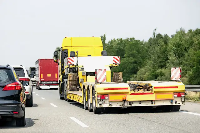 Korek na autostradzie, żółta ciężarówka z niskopodwoziową naczepą i czerwony tir. Zakaz dla ciężarówek w tym miejscu?