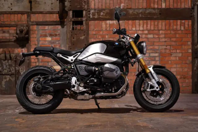 Stylowy motocykl BMW R nineT, jeden z klasycznych naked bikes, z błyszczącym, czarnym bakiem i złotym widelcem, na tle ceglanej ściany.