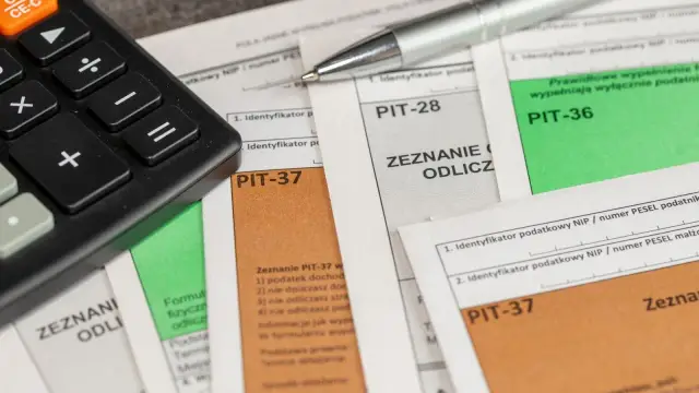 Kalkulator i długopis leżą na dokumentach PIT-37, PIT-28 i PIT-36. Czas na rozliczenie podatku i ewentualną darowiznę.