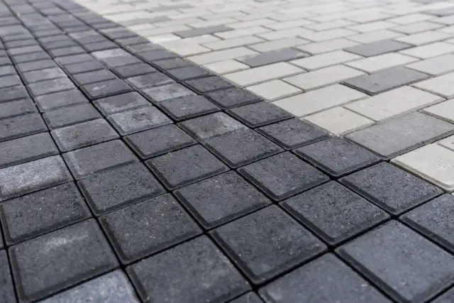 Szara i biała kostka brukowa ułożona w geometryczny wzór. Zastanawiasz się, ile kostki na m2?
