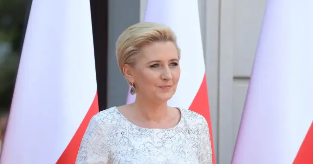 Pierwsza dama w białej sukni z kwiatowym wzorem, obok flagi Polski.