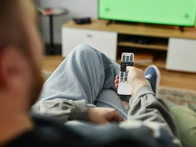Osoba z pilotem w ręku, gotowa do oglądania telewizji. Czas pomyśleć o abonamencie RTV 2025.