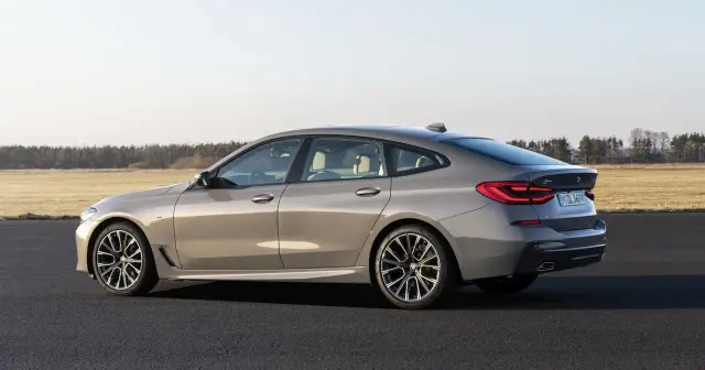 Eleganckie, szare BMW GT z jasnym wnętrzem stoi na asfalcie. W tle rozciąga się pole i las.