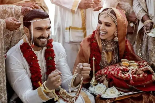 Para hinduskie wesele: pan młody w białej sherwani, panna młoda w czerwonym sari. Wskazówka, jak się ubrać na hinduskie wesele, to bogate zdobienia i żywe kolory.