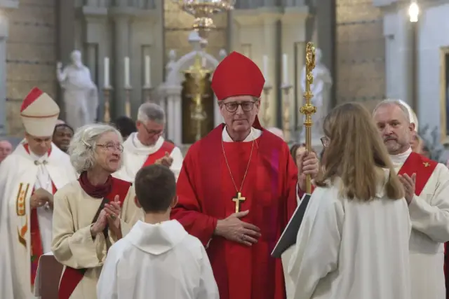 Biskup w czerwonej szacie i mitrze, z pastorałem, podczas uroczystości. Różnice między kościołem starokatolickim a rzymskokatolickim są widoczne w liturgii.