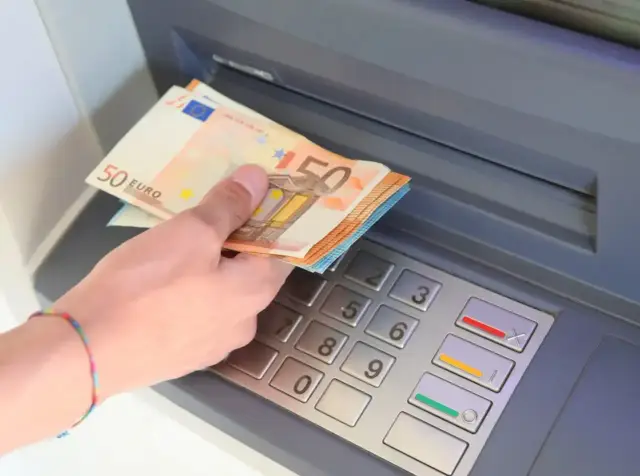 Dłoń trzyma banknoty 50 euro przy bankomacie. W Hiszpanii obowiązuje euro, więc to typowa waluta do wypłaty.