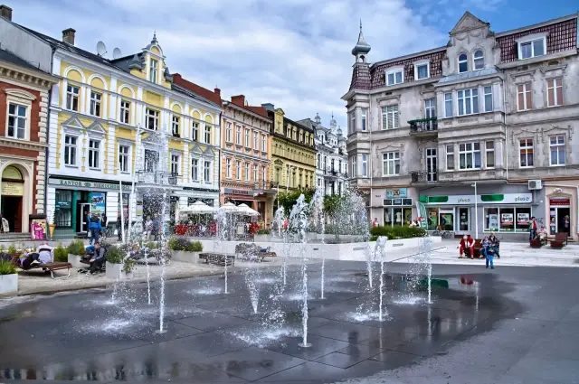 Urokliwy plac z fontannami w świnoujście stare miasto. Kolorowe kamienice, ludzie odpoczywający na ławkach i letnia atmosfera.
