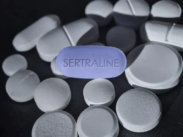 Fioletowa tabletka z napisem SERTRALINE wśród białych tabletek. Zotral 50 pomaga w walce z depresją.