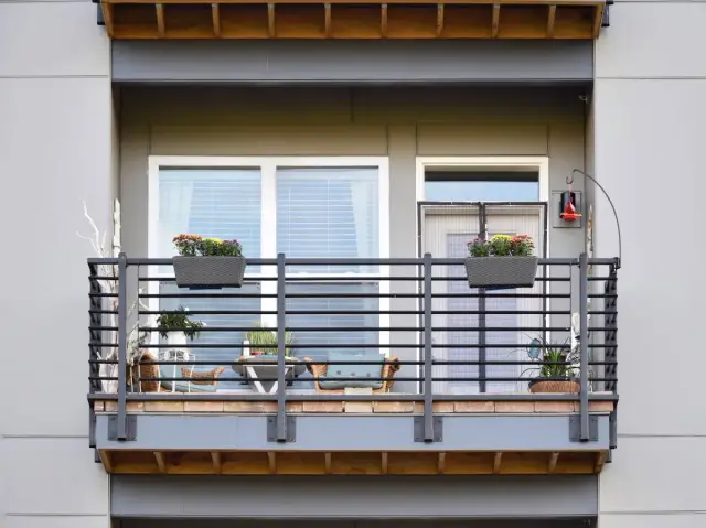 Nowoczesny balkon dostawny do domu jednorodzinnego z meblami i kwiatami.