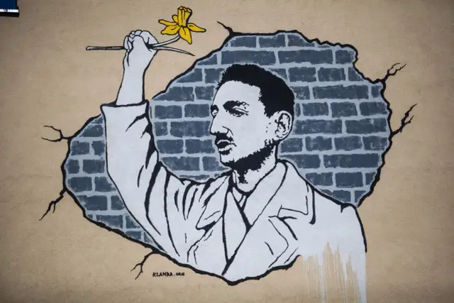Murale przedstawia mężczyznę z żółtym kwiatem, który przebija się przez ceglaną ścianę. To jeden z bohaterów, którzy chcą zdążyć przed panem bogiem.