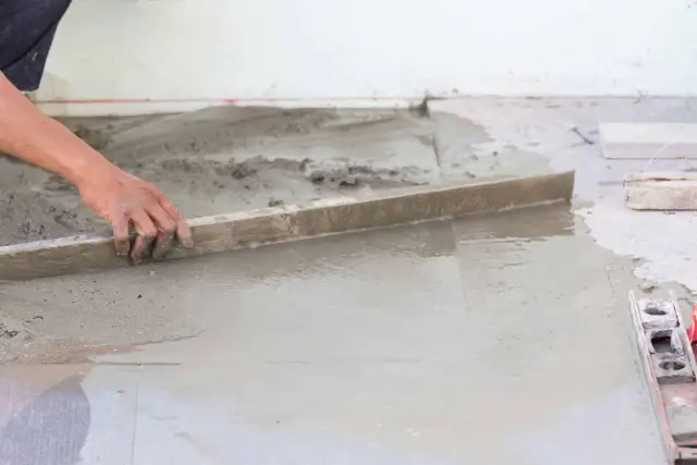 Ręka wyrównuje świeży, gotowy beton na posadzkę za pomocą łaty.