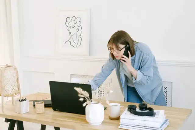 Wirtualna asystentka w okularach rozmawia przez telefon, pracując przy laptopie.