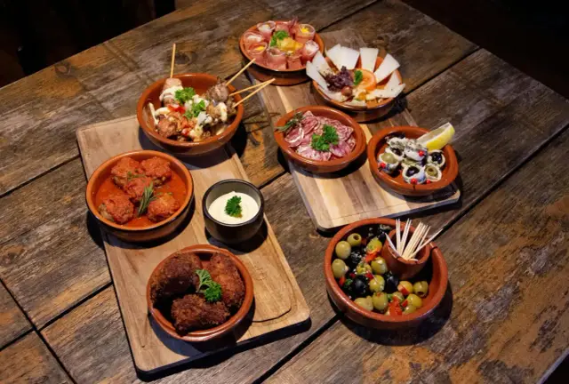 Pyszne hiszpańskie jedzenie: tapas, oliwki, ser i mięsne kulki na drewnianym stole.