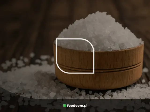 Górka kryształków soli, czyli chlorku sodu, w drewnianej miseczce na ciemnym tle.