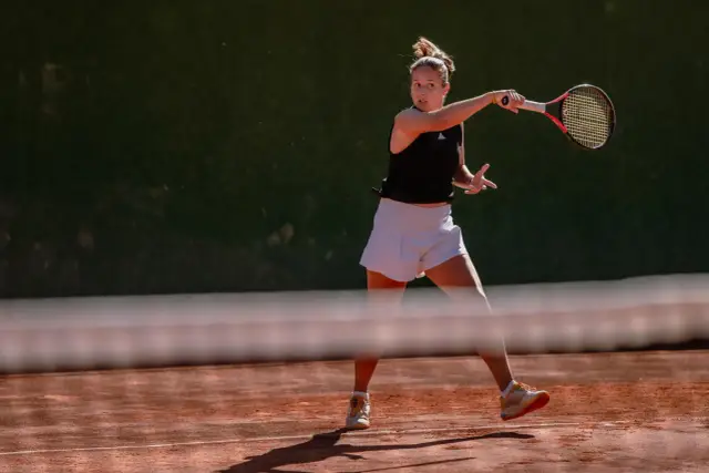 Tenisistka wykonuje potężny backhand na ceglanym korcie.
