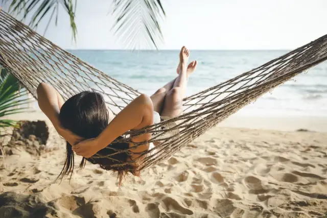 Kobieta odpoczywa w hamaku na plaży, ciesząc się dodatkowym urlopem. W tle widać morze i palmy.
