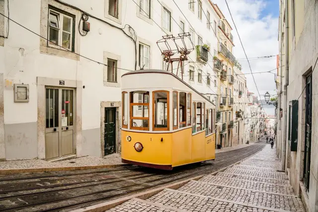 Żółty tramwaj zjeżdża po brukowanej ulicy w Lizbonie, stolicy nad estuarium Tagu.