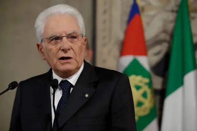 Sergio Mattarella, prezydent Włoch, przemawia na tle flag.
