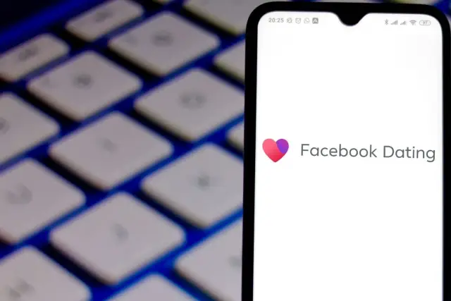 Ekran telefonu z logo Facebook Dating na tle klawiatury.