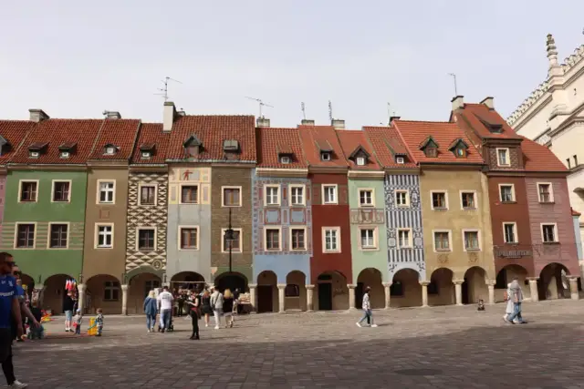 Kolorowe kamienice na Starym Rynku w Poznaniu. Co ciekawego w Poznaniu? Tętniący życiem plac, ludzie spacerujący pod arkadami.