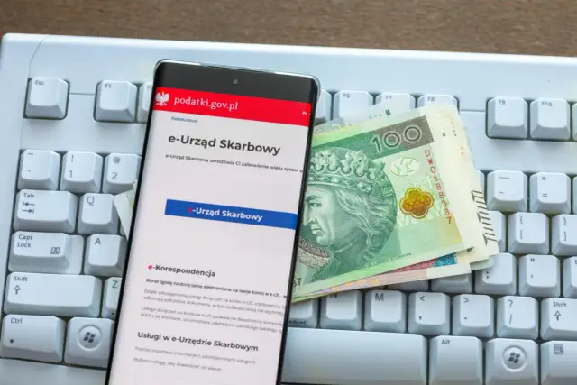Na klawiaturze leży smartfon z aplikacją e-Urząd Skarbowy i polskie banknoty. Sprawdź, jak sprawdzić, czy podatek od nieruchomości został zapłacony.