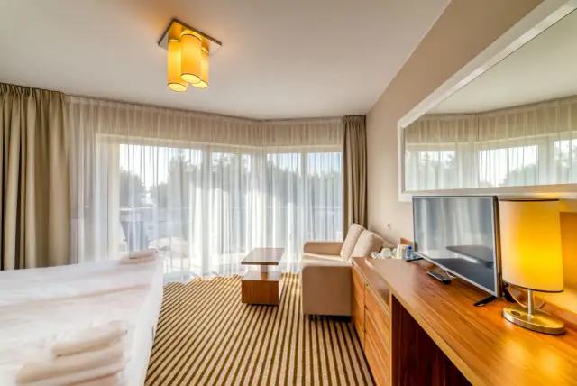 Przytulny pokój z widokiem na morze. Jasne zasłony, wygodna sofa i łóżko czekają na gości. Wolne pokoje nad morzem to idealne miejsce na relaks.