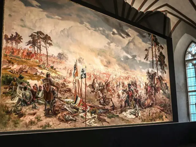 Monumentalne malowidło przedstawia bitwę pod Grunwaldem. Widać chaos walki, rycerzy na koniach, chorągwie i poległych.