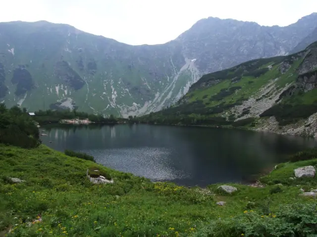 Ciemne jezioro górskie otoczone zielonymi zboczami i skalistymi szczytami.
