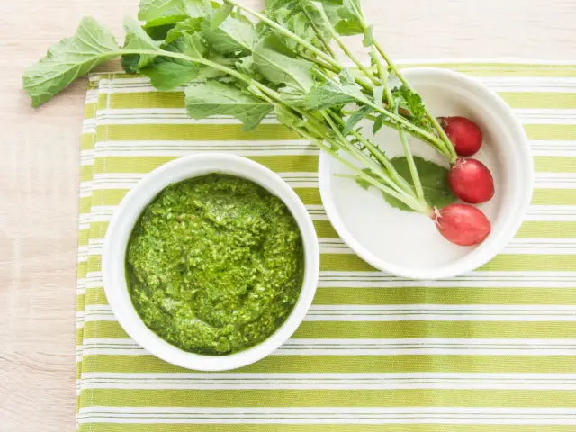 Pesto z liści rzodkiewki, świeże rzodkiewki i zielone liście na zielono-białym tle.
