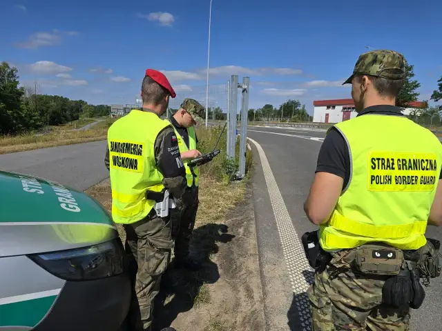 Strażnicy graniczni w kamizelkach odblaskowych sprawdzają dokumenty przy granicy państwowej.